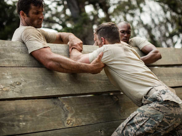 soldiers helping man to climb wooden wall in boot camp